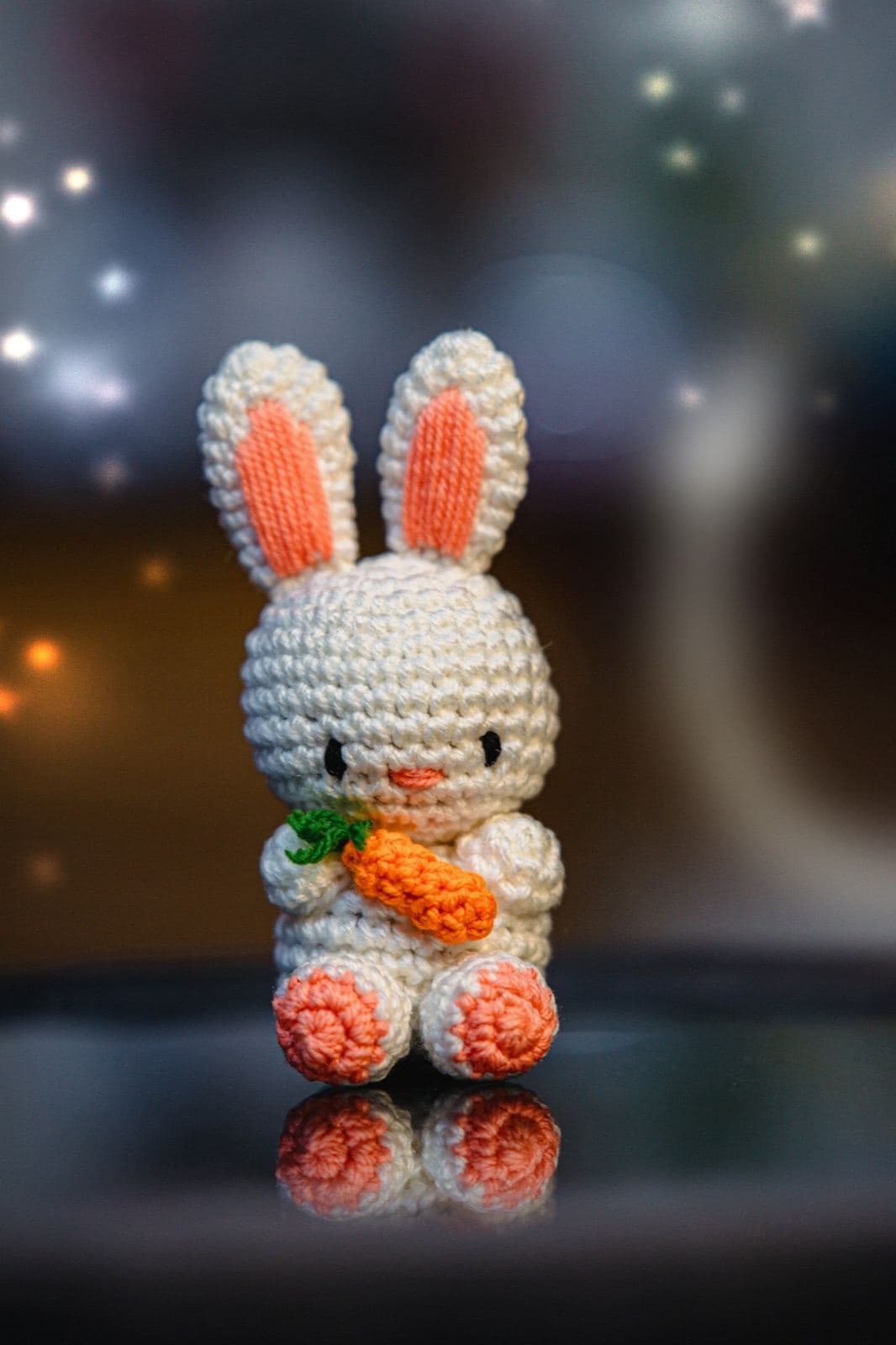 A cream crochet amigurumi bunny with peach ears holding a small crochet carrot