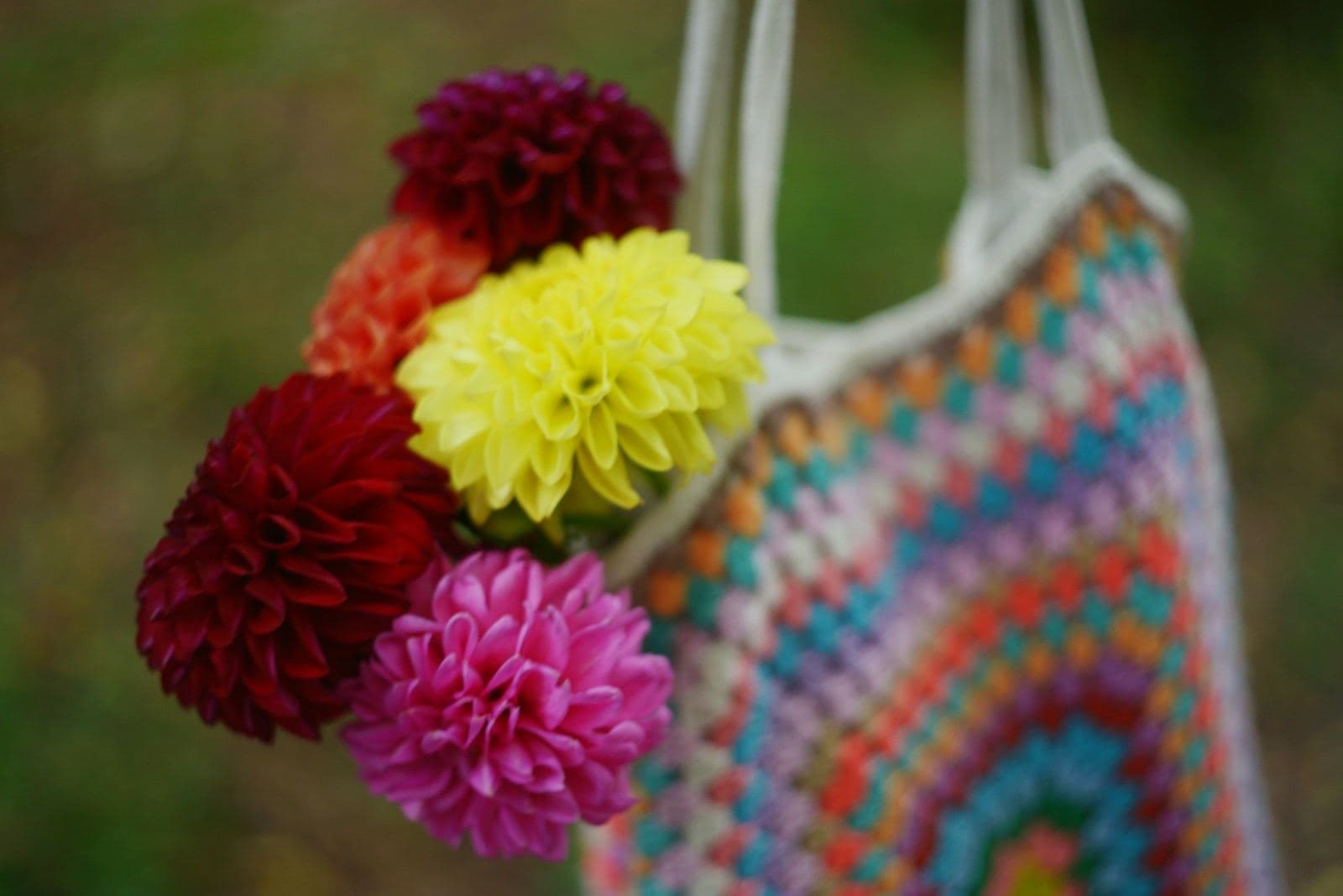 A colorful granny-stitch crochet tote holding a bouquet of dahlias