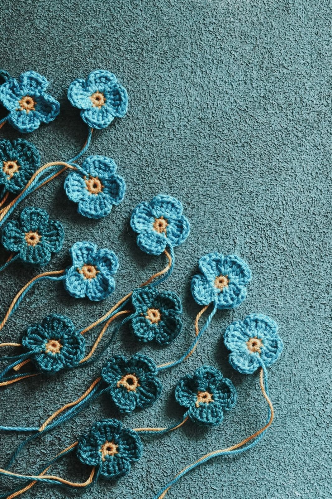 Small blue crochet flowers with yellow centers scattered on a teal background