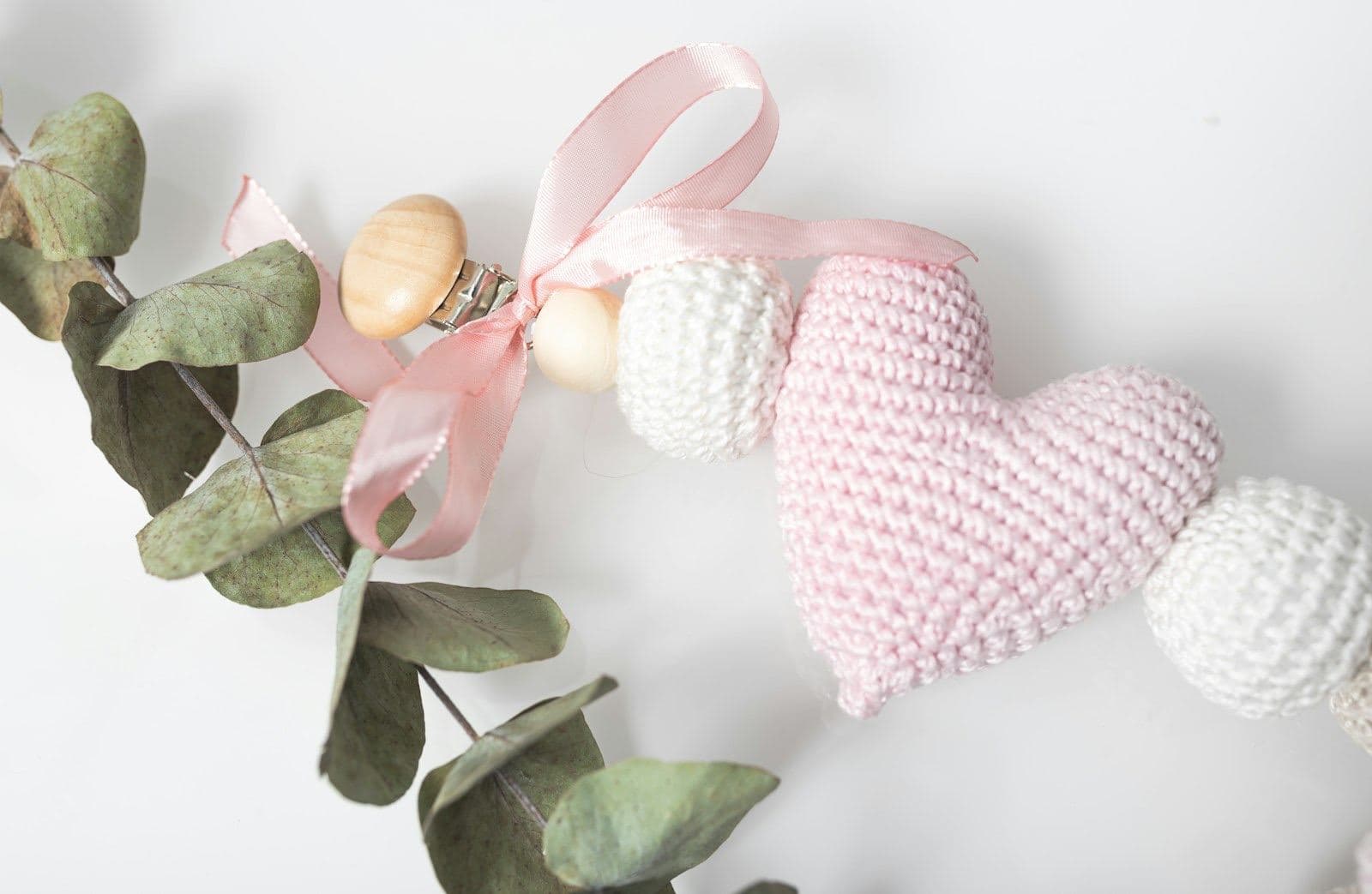 A puffy pale pink crochet heart on a string of white crochet beads with a pink ribbon and eucalyptus