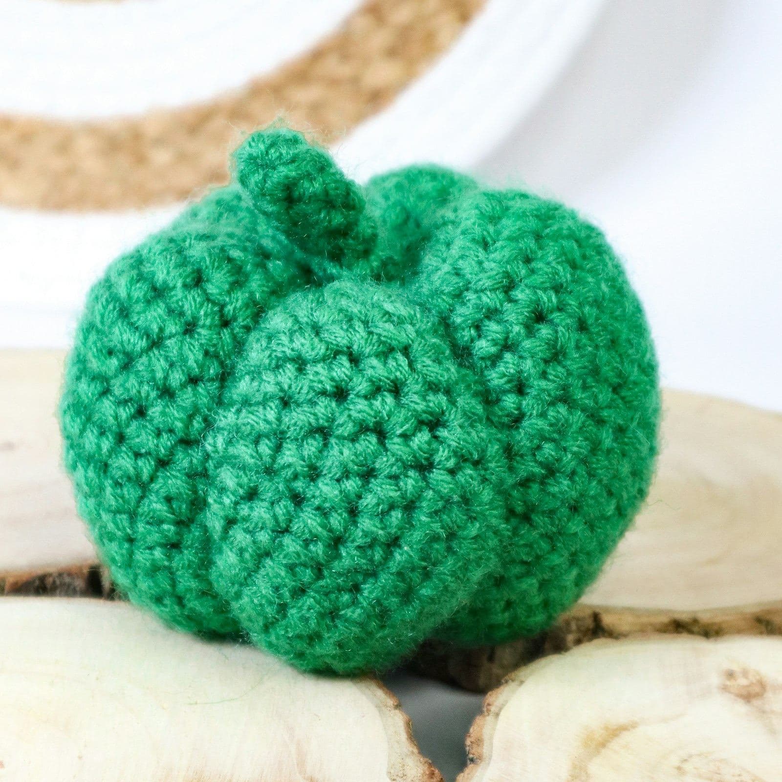 A green crochet pumpkin with a short stem sitting on wood slices