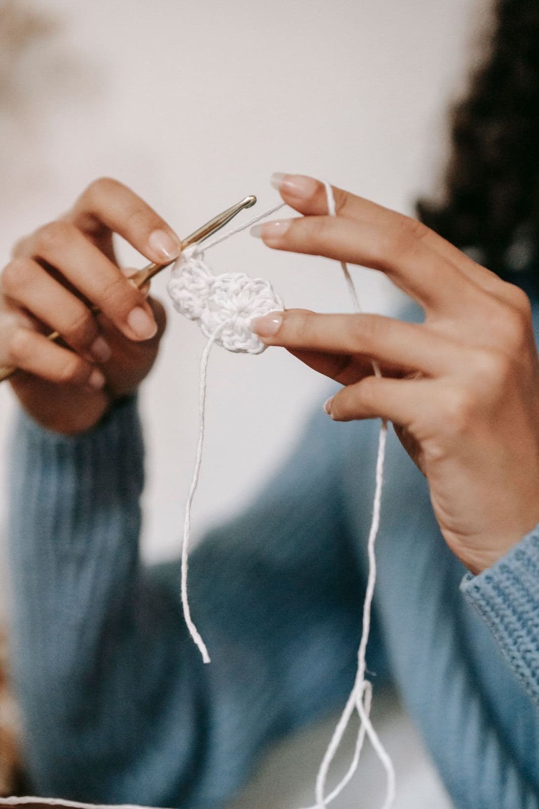 Hands working the first round of a small white crochet circle with a metal crochet hook