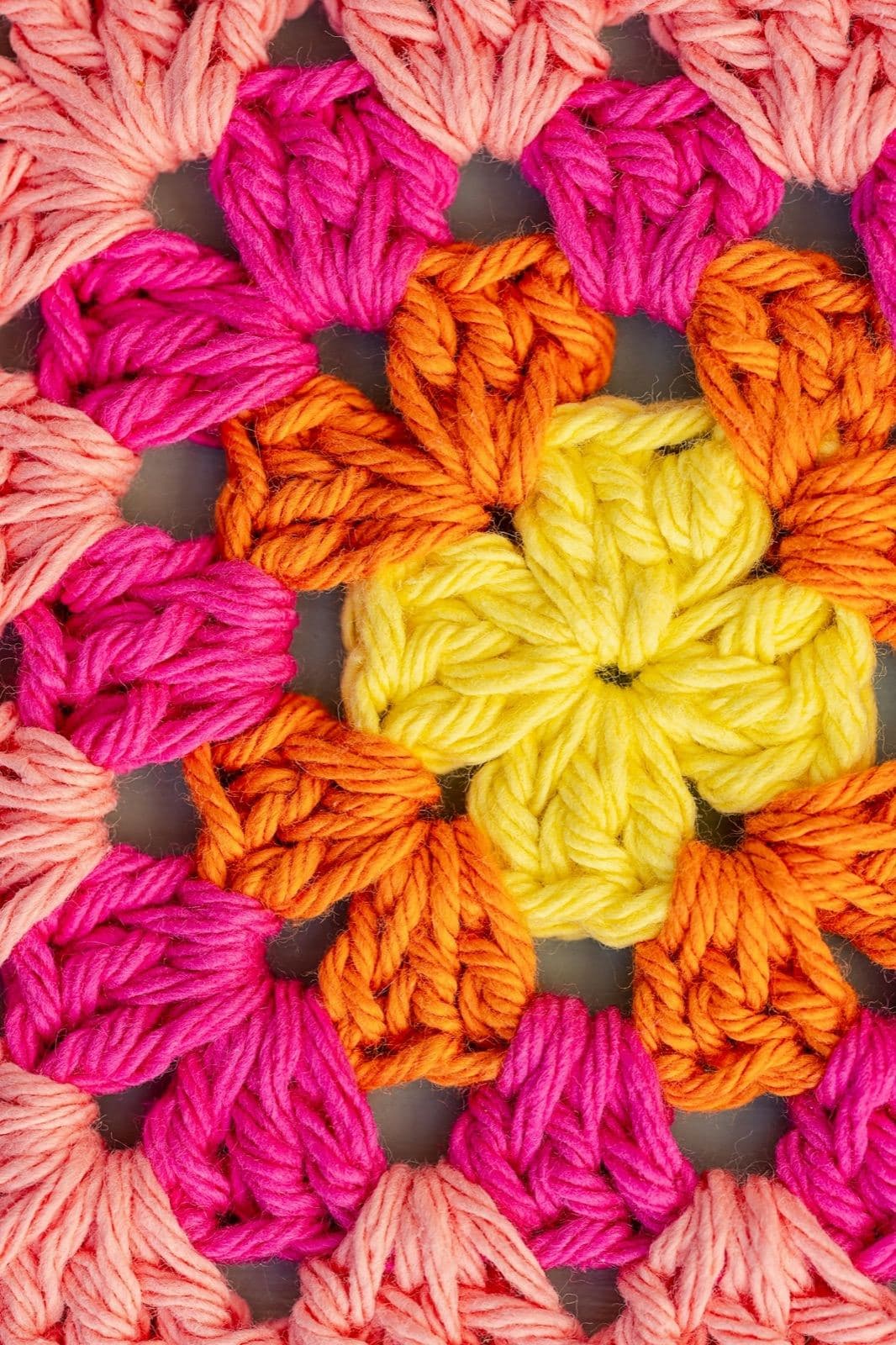 Close-up of a bright crochet granny square in yellow, orange, and pink