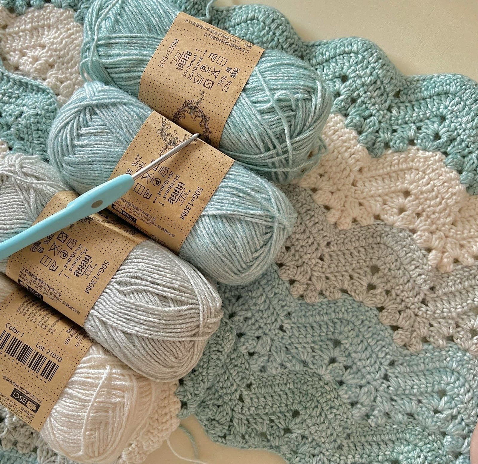 Skeins of pale blue and cream cotton yarn with a crochet hook on a chevron crochet blanket