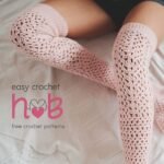 Handmade crochet knee high socks in gray yarn displayed on crossed legs resting on a cozy bed
