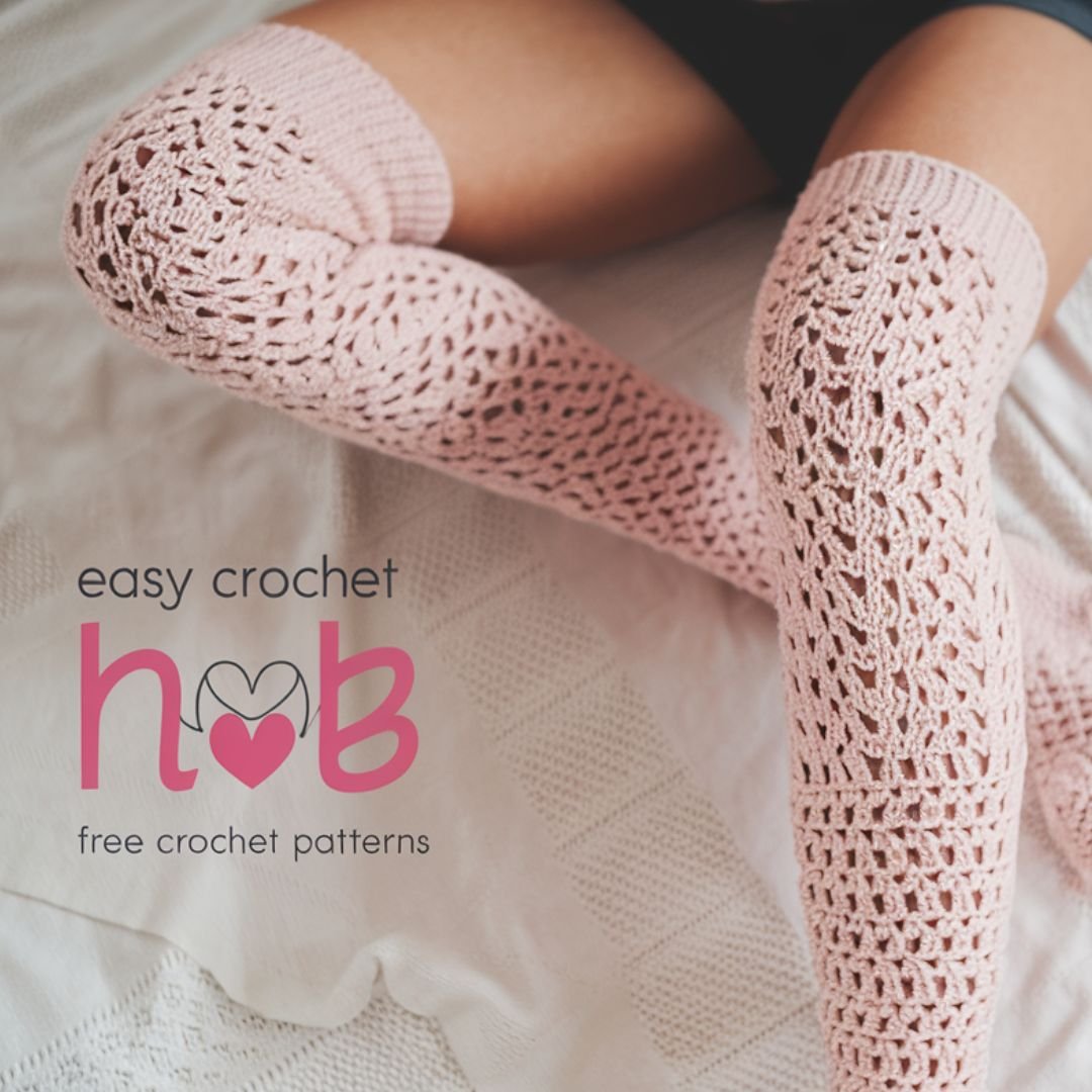 Handmade crochet knee high socks in gray yarn displayed on crossed legs resting on a cozy bed